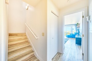 A hallway with a wooden staircase, a white door, and a view into a living area with blue furniture.