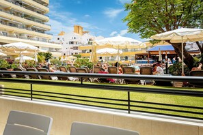 A poolside area with multiple lounge chairs and umbrellas, a pool, and a building with balconies in the background. - Great Location Santa Maria Studio . Pool view.Fully refurbished.Air con. WIFI (Costa Adeje)