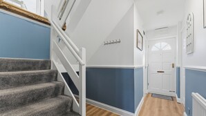Eine Treppe mit weißer Handlauf, die zu einer Empfangshalle mit Garderobe führt.