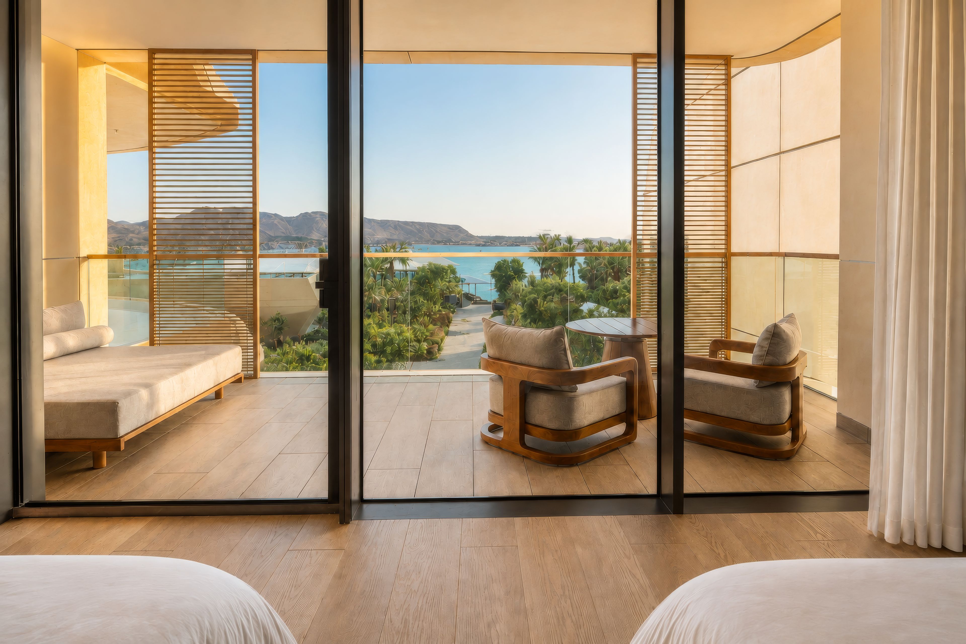 A balcony with a view of a body of water, a seating area with a table, and a bed.
