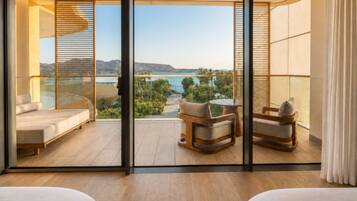 A balcony with a view of a body of water, a seating area with a table, and a bed.