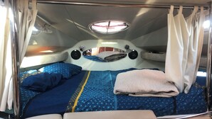 Un interior compacto y bien iluminado con una cama que presenta un edredón estampado con un diseño geométrico, un cabecero con un espejo circular y una pequeña lámpara sobre la cama.