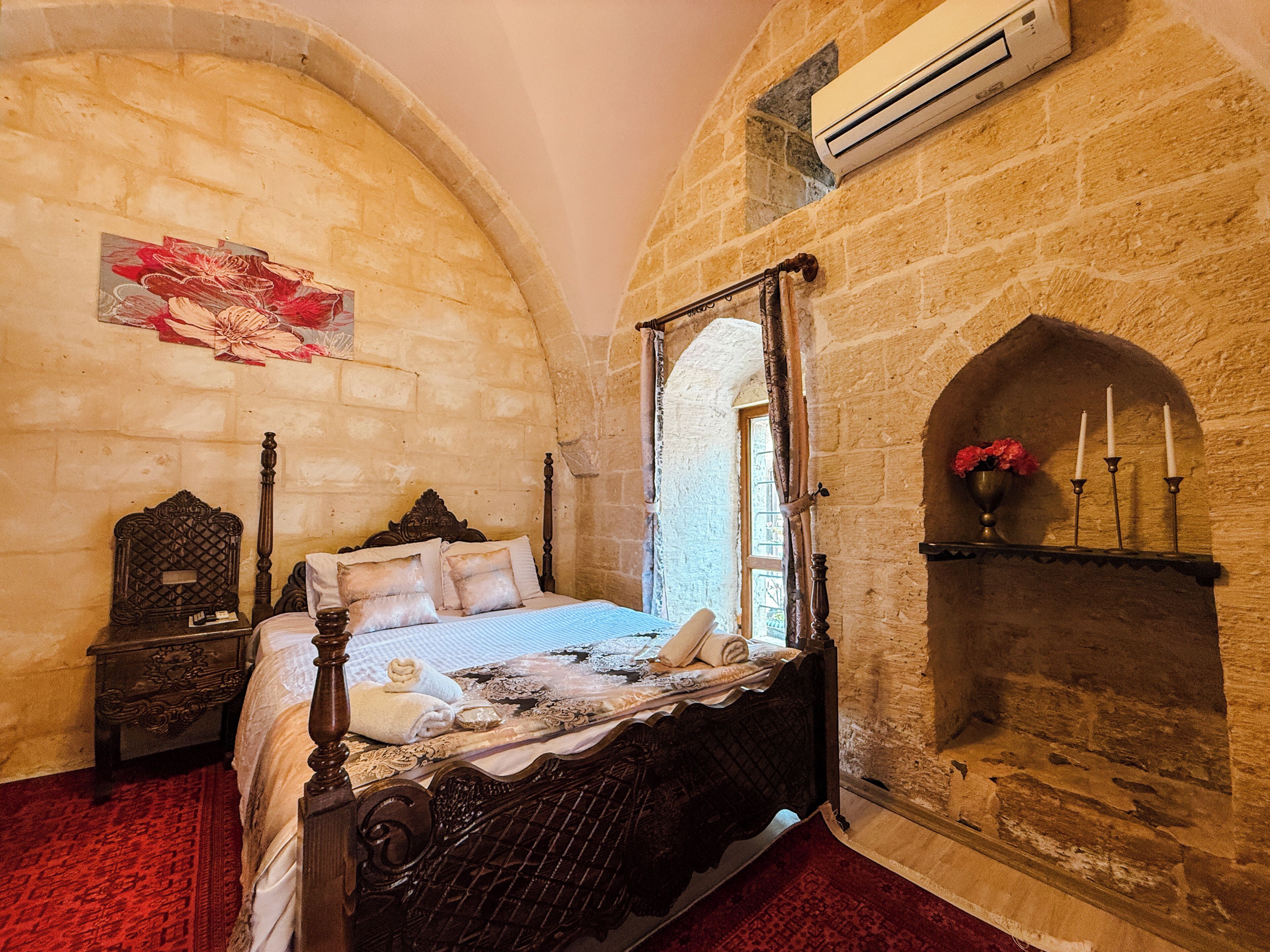 A room with a stone wall, a bed with a canopy, a fireplace, and a window.