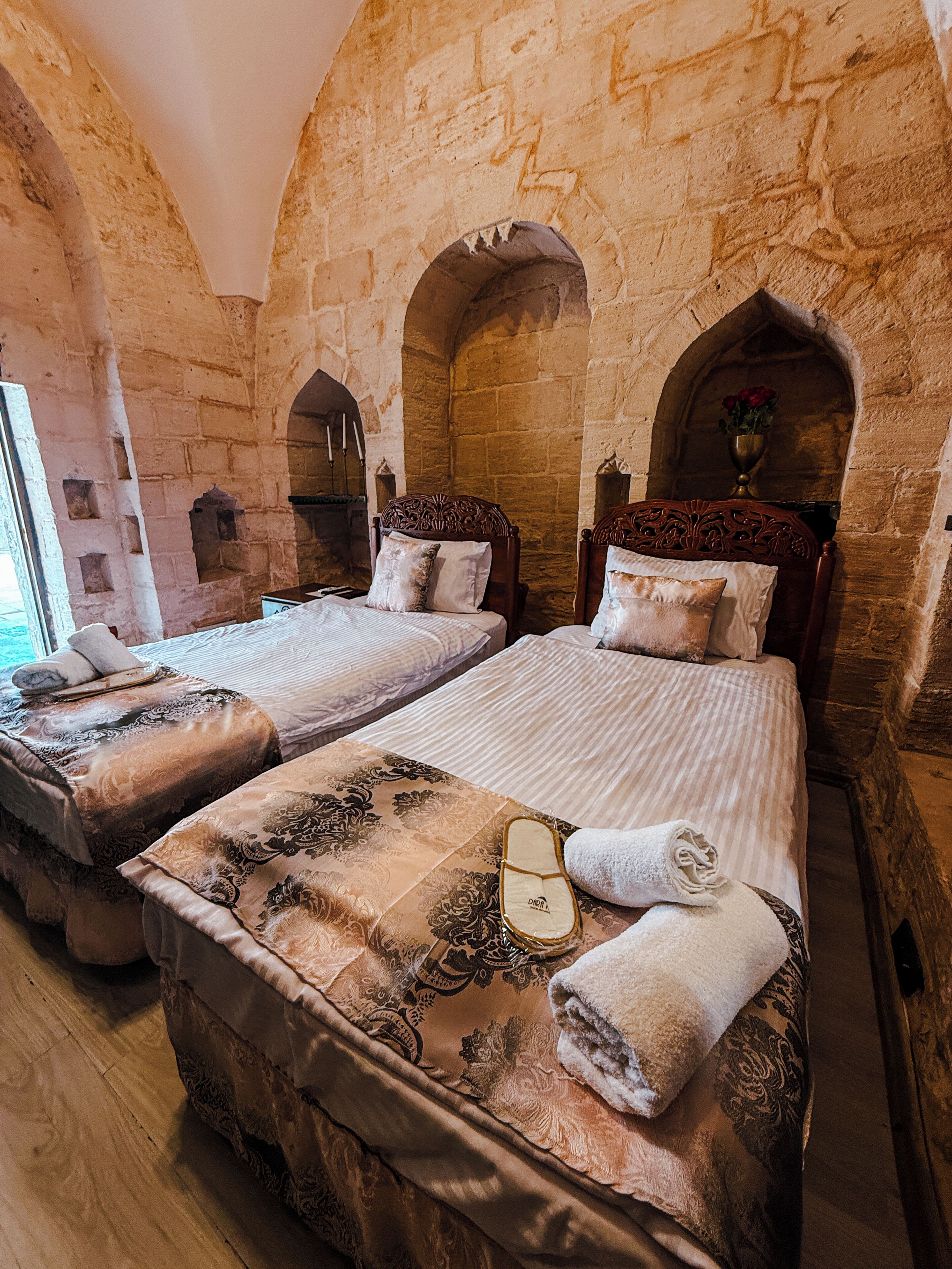A room with two beds, stone walls, and a window.
