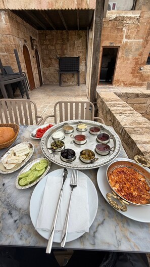 A table set outdoors with various dishes, a bench, and stone walls in the background. - DARA KONAĞI (Mardin)