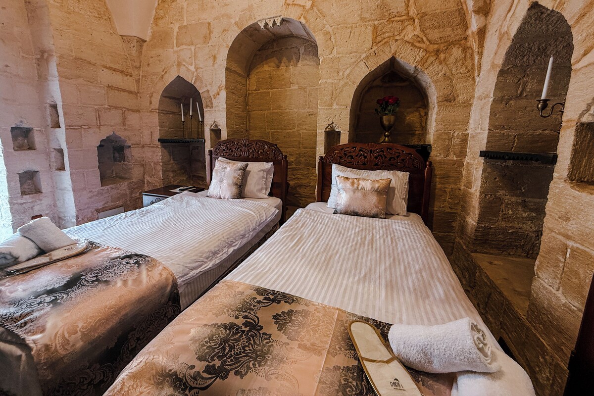 A room with two beds, stone walls, and arched doorways.