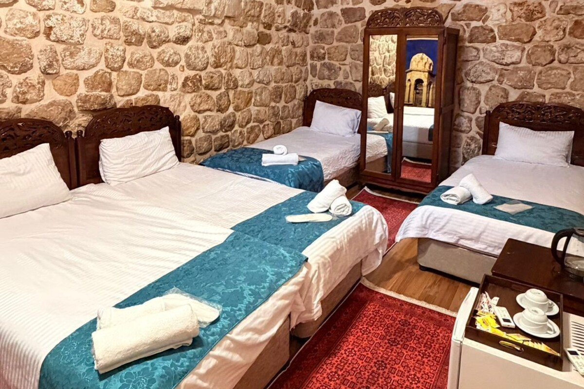 A hotel room with two beds, a red patterned rug, stone walls, and a wooden dresser with a tray.