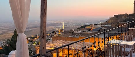 A balcony with a view of a cityscape at dusk, featuring a railing and a patterned carpet.