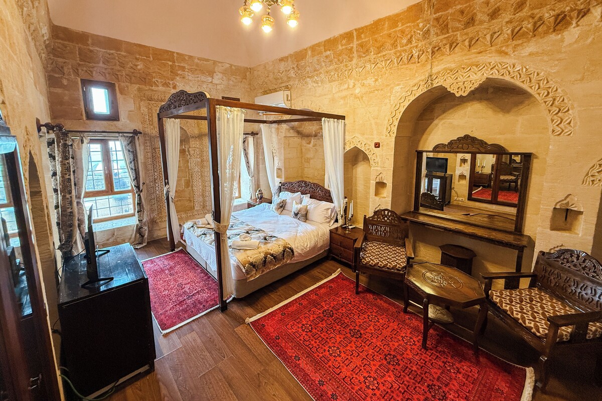 A room with a four-poster bed, a red rug, a wooden chair, and a mirror on the wall.