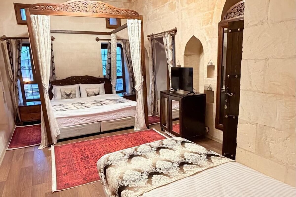 A bedroom with a large bed, a smaller bed, a TV, and a stone wall.