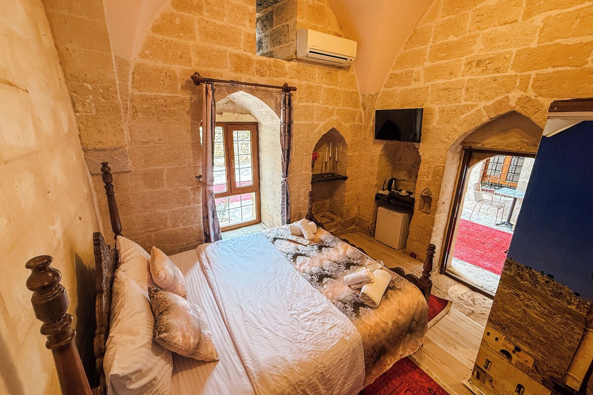 A room with a bed, a small desk, an air conditioning unit, a television, and a window with a view of the outside.