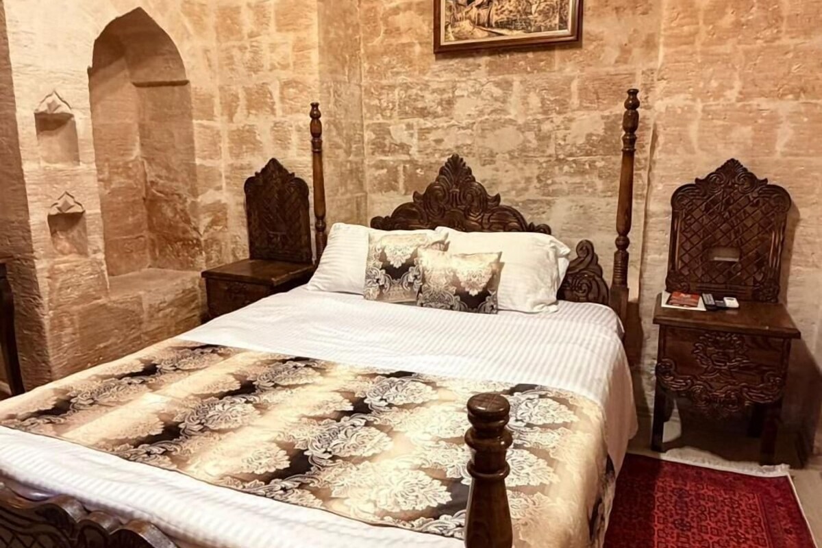 A room with a large bed, a red patterned rug, stone walls, and a framed picture on the wall.