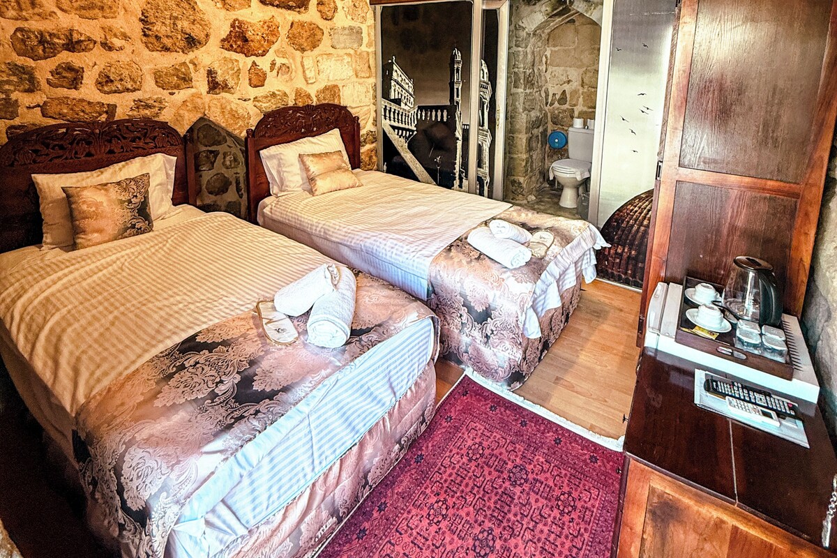 A room with two beds, a wooden wardrobe, and stone walls.