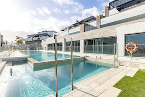 Ein Schwimmbecken mit klarem Wasser, umgeben von einem modernen Gebäude mit großen Fenstern und einer Stein-Fassade.