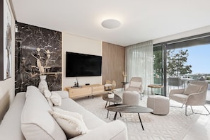 Ein modernes Wohnzimmer mit einer Couch, einem Couchtisch, einem Fernseher und einem Balkon mit Sitzgelegenheit.