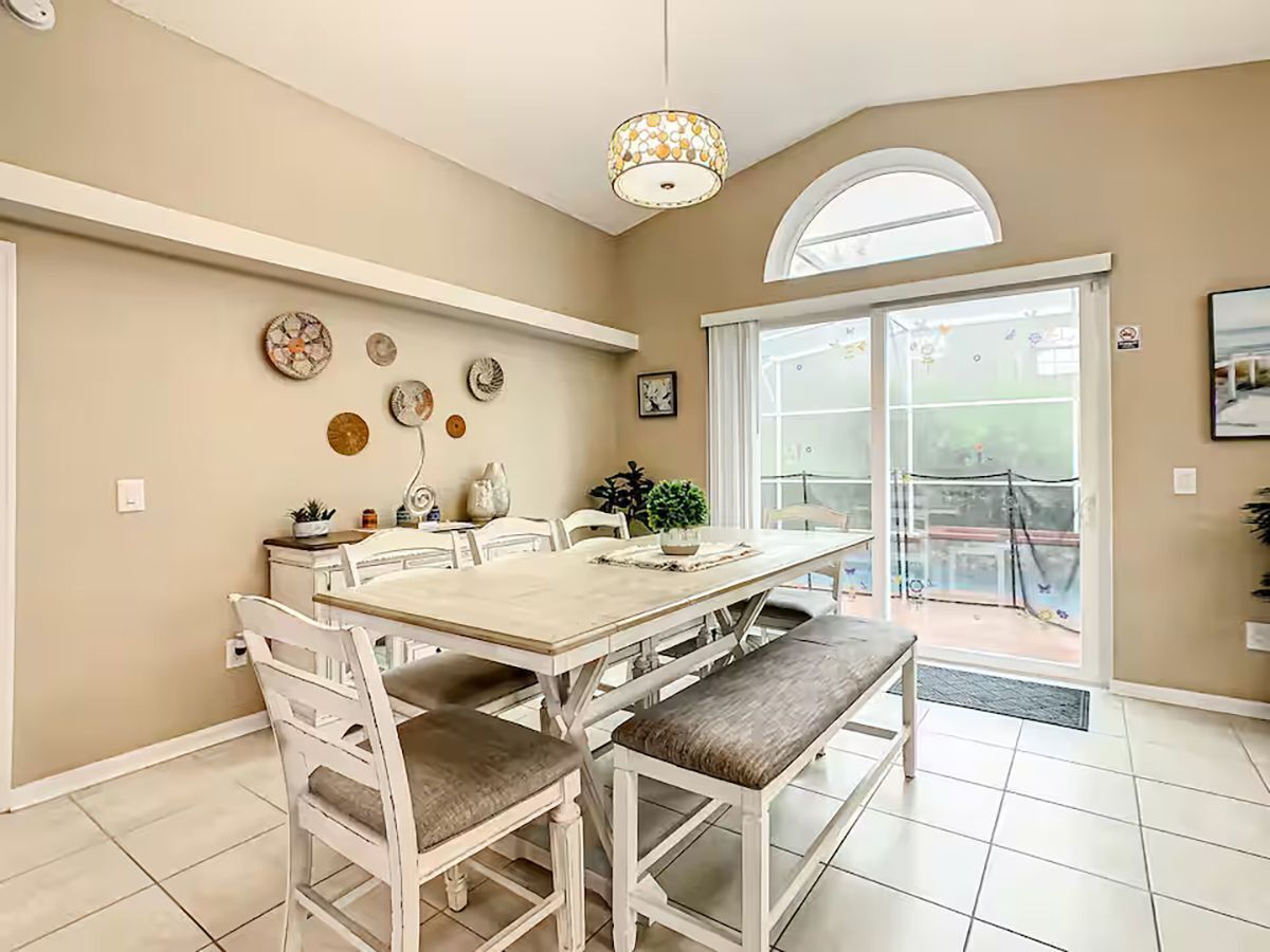 A dining area with a table, chairs, and a bench. There is a ceiling light fixture, a window, and a door leading outside.