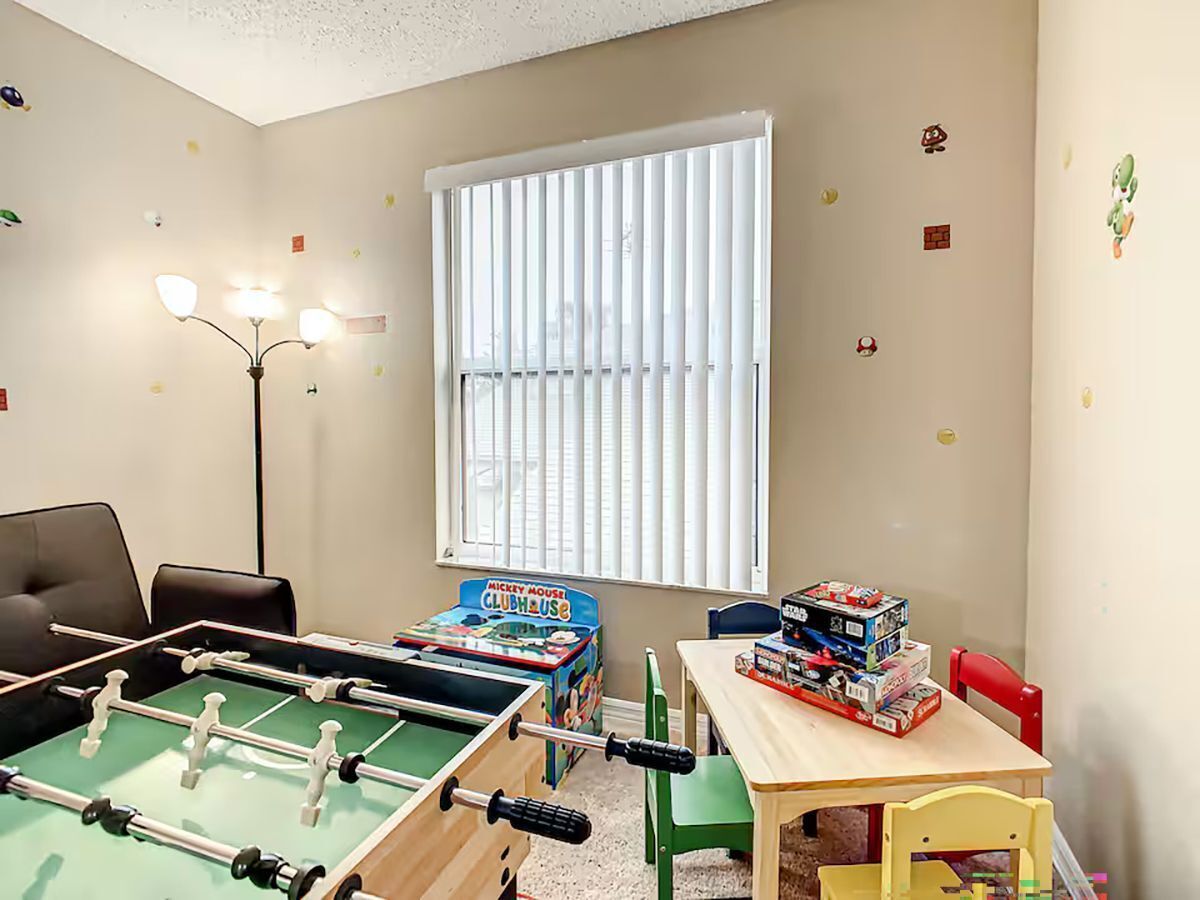 Ein Zimmer mit einer Tischfußballplatte, einem Mickey Mouse Clubhouse Spiel und einem Fenster mit Jalousien.