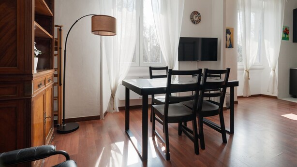Un comedor con una mesa y sillas, una lámpara de pie y un televisor en la pared.