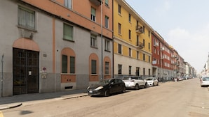 Una calle con coches aparcados, edificios con ventanales de arco y cielo despejado.