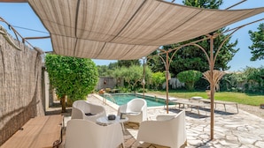 Un área de estar al aire libre con techo, piscina, suelo de piedra y pérgola.