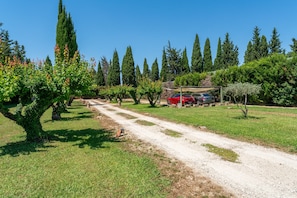 A dirt path leading through a landscaped area with trees and shrubs, a car parked under a shaded structure, and a clear blue sky. - Holiday Home 'Mas St Anne' with Private Pool, Wi-Fi and Air Conditioning (Saint-Étienne-du-Grès)