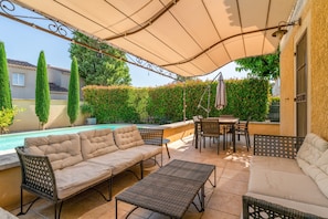 A covered outdoor patio with a pool, seating, and a table.