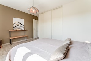 A bedroom with a bed, a bench, a hanging light fixture, a wardrobe, and a painting on the wall.