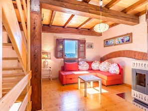 Un salon chaleureux avec un escalier en bois, un canapé rouge, une petite table et une cheminée.
