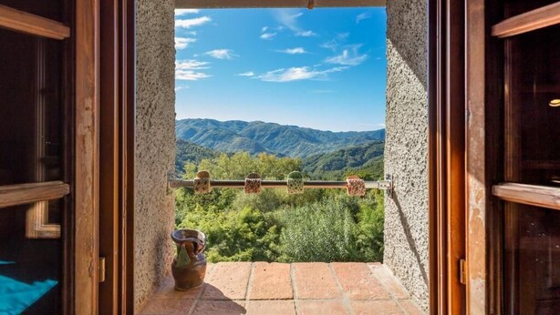 A view from a balcony with a rustic stone wall, a metal railing, and a small vase on the floor. - Casa dei Ciliegi (Bagni di Lucca)