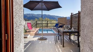 An outdoor pool area with a view of mountains, a table with chairs, and a large umbrella. - Casa dei Ciliegi (Bagni di Lucca)