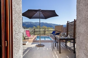 An outdoor pool area with a view of mountains, a table with chairs, and a large umbrella.