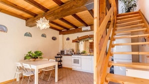 A kitchen with a wooden staircase, a dining table with chairs, and a potted plant. - Casa dei Ciliegi (Bagni di Lucca)