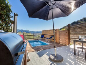 Un espace aménagé au bord de la piscine, avec un barbecue, des chaises longues et une vue sur les montagnes.