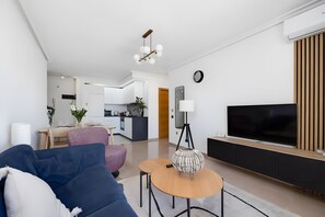 A modern living room with a sofa, a TV, and a dining area in the background. - Apartment with Sea View, 300m from the Beach (La Mata)