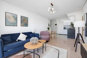 A modern living room with a blue sofa, a round coffee table, and a kitchen in the background. - Apartment with Sea View, 300m from the Beach (La Mata)