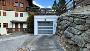 A building with a garage entrance, stone wall, and a wooden balcony. - ALPINE VIEW Apartment Bad Kleinkirchheim (Bach)