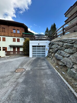 A building with a garage entrance, stone wall, and a wooden balcony. - ALPINE VIEW Apartment Bad Kleinkirchheim (Bach)