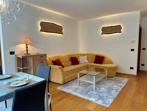 A living room with a sofa, a glass coffee table, a dining table with plates, a lamp, and wall-mounted light fixtures. - ALPINE VIEW Apartment Bad Kleinkirchheim (Bach)