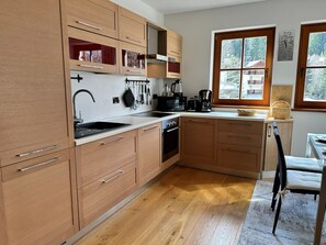 A kitchen with wooden cabinets, a sink, a stove, and a window with a view of trees. - ALPINE VIEW Apartment Bad Kleinkirchheim (Bach)