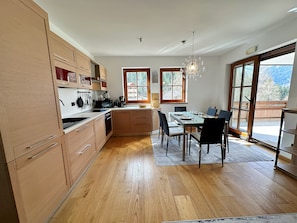 A modern kitchen with wooden cabinets, a dining table with chairs, and a large window with a view of the outdoors. - ALPINE VIEW Apartment Bad Kleinkirchheim (Bach)