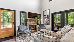 Amplia sala de estar con chimenea de piedra, asientos cómodos y ventanas grandes con vistas al exterior.