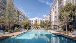 A rectangular swimming pool with lounge chairs and trees, surrounded by multi-story buildings. - New 2-bedroom corporate loft in charming Atlanta, right by the airport. (Atlanta)