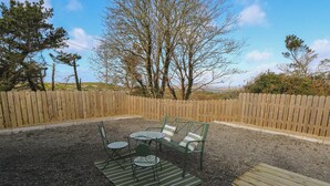 An outdoor seating area with a table and chairs, a wooden bench, and a gravel ground. - Red House (Carraroe)