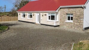 A two-story house with a red roof, stone exterior, and a gravel driveway. - Red House (Carraroe)