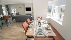 A dining area with a table set for four, a sofa, and a TV in the background. - Red House (Carraroe)