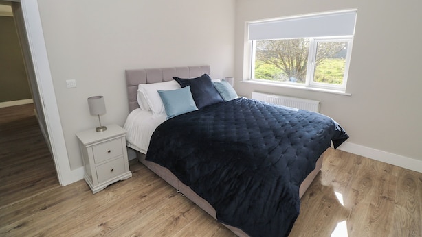 A bedroom with a bed, bedside table, and a window. - Red House (Carraroe)