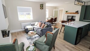 A modern living room with a grey sofa, green armchairs, a small coffee table, and a kitchen area with a bar counter. - Red House (Carraroe)