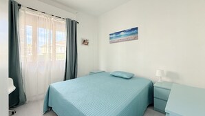 Une chambre à coucher avec un lit, une table de chevet, une lampe, une fenêtre avec des rideaux et un tableau au mur.