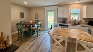 Una cocina compacta con armarios blancos, un comedor con mesa y sillas de madera, y una puerta que da a un patio.