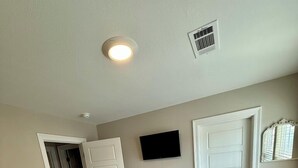 Un dormitorio con cama, televisor, puerta y rejilla de ventilación.